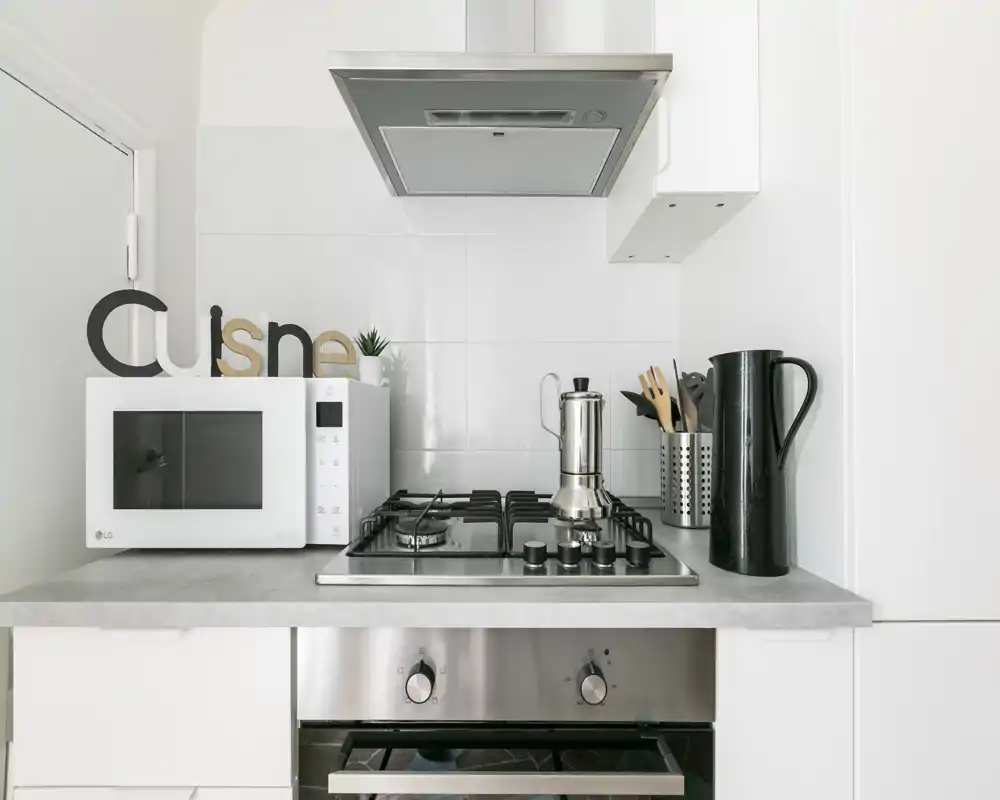 Angolo cucina moderno e luminoso con piano cottura a gas, cappa, microonde e accessori sul piano ordinati; stile minimal e pulito, perfetto per annunci.