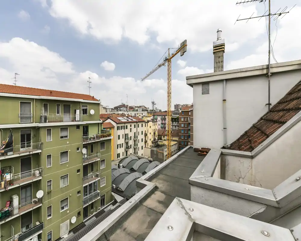 Veduta dal tetto/terrazza su palazzi residenziali e una gru, con cielo sereno e skyline urbano — perfetta per presentare uno spazio esterno in città.