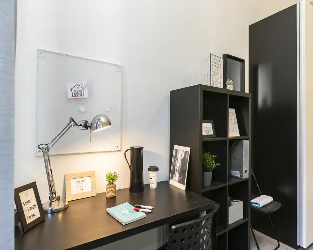 Angolo studio ben organizzato con scrivania nera, lampada regolabile in metallo e scaffale: accogliente e funzionale per smart working o lettura.