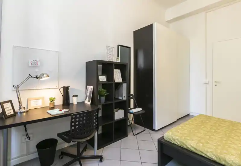 Dormitorio luminoso y bien presentado con cama individual, armario y un rincón de estudio ordenado con escritorio y estantería—ideal para estudiante o persona sola.