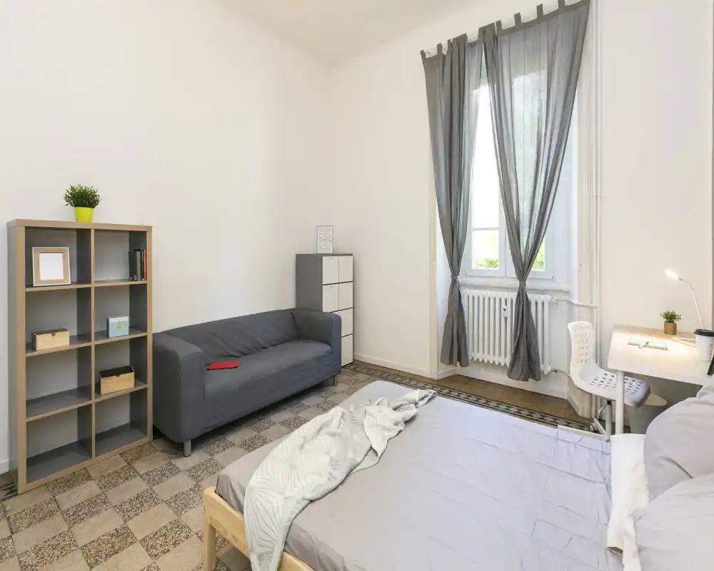 Dormitorio luminoso y de estilo sencillo con cama doble, escritorio y un pequeño sofá junto a la ventana — líneas limpias y luz natural lo hacen acogedor.