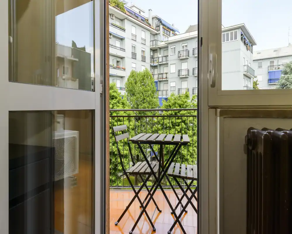 Petit balcon privé avec une table bistro pliante et deux chaises, donnant sur la verdure et les immeubles voisins — idéal pour un café matinal.