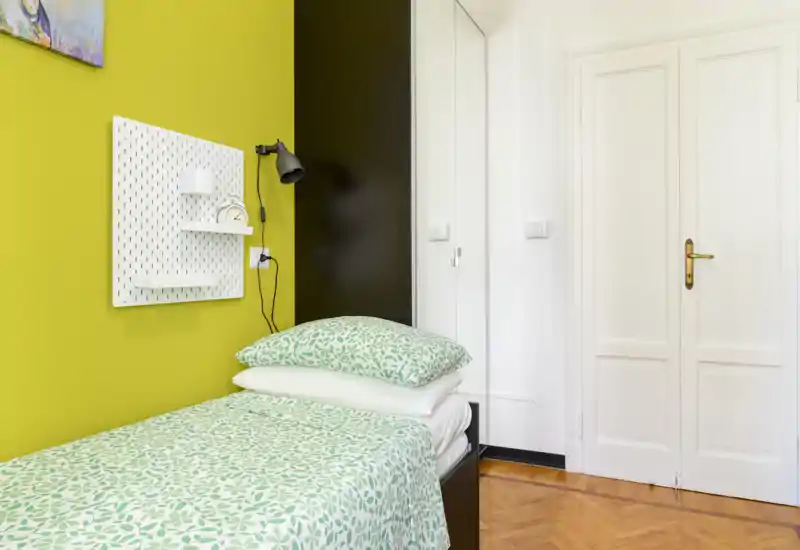 Camera singola luminosa e ben arredata con parete verde, biancheria a fantasia e pavimento in parquet; spazio compatto e funzionale perfetto per ospiti o affitti brevi.