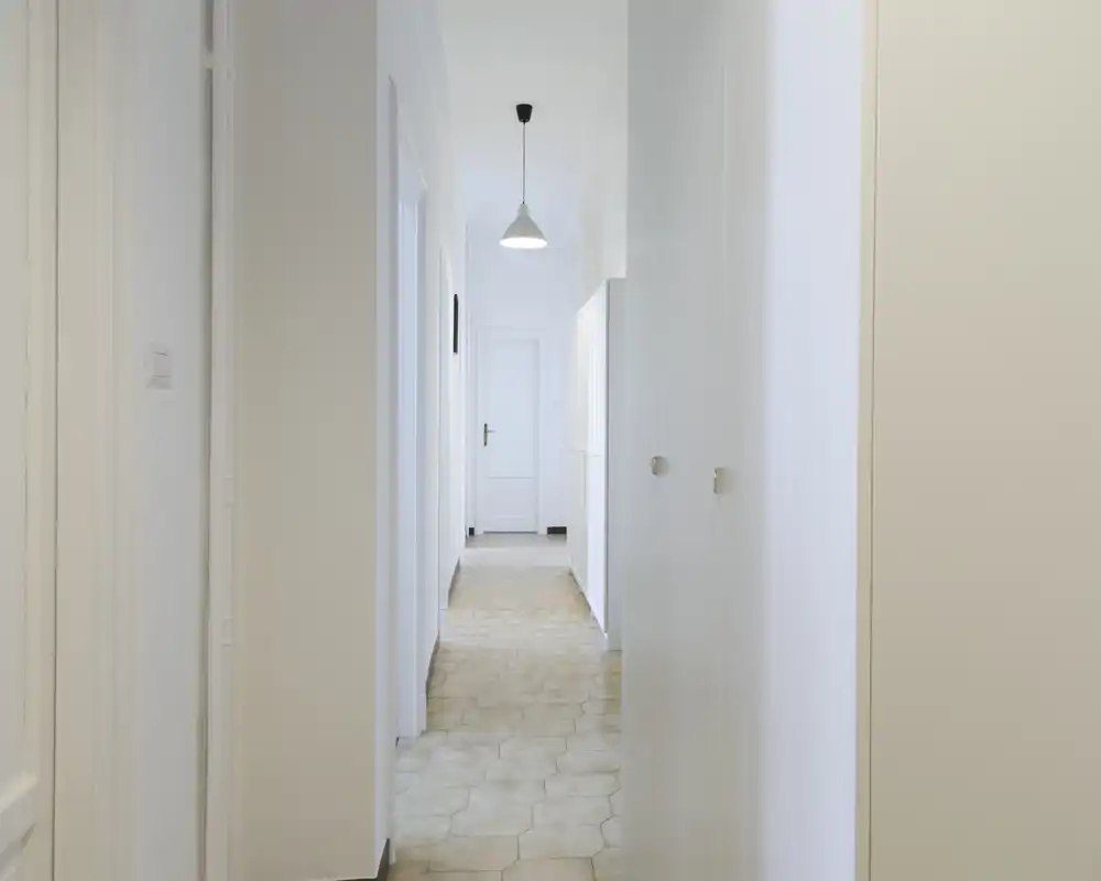 Corridoio d'ingresso luminoso e minimale con pavimento esagonale, pareti bianche e una lampada a sospensione; corridoio pulito che conduce alle porte interne.