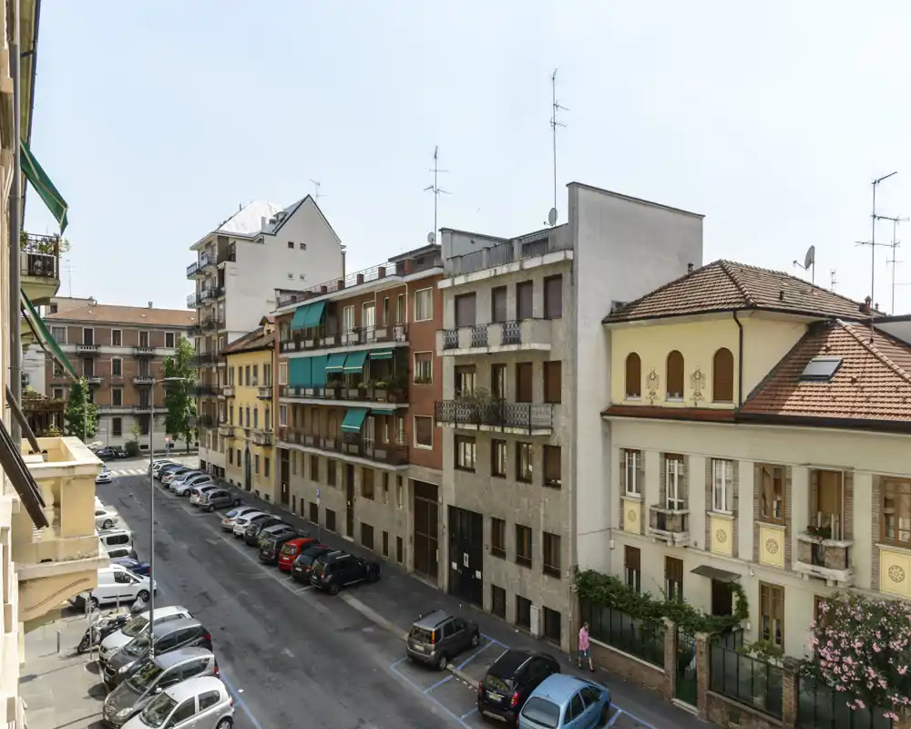 Vista soleggiata dalla balconata su edifici residenziali e auto parcheggiate — ideale per mostrare l’affaccio esterno e il contesto del quartiere.