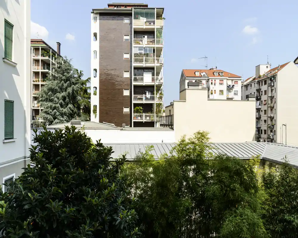 Vista urbana gradevole con condomini vicini e vegetazione in primo piano, ripresa in pieno giorno — ideale per mostrare il panorama da un balcone o finestra.