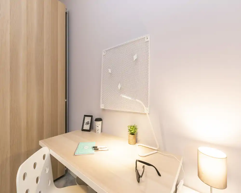 Angolo scrivania luminoso e ben arredato in un'area giorno, con lampada, pianta e armadio vicino — ideale per lavoro o studio.