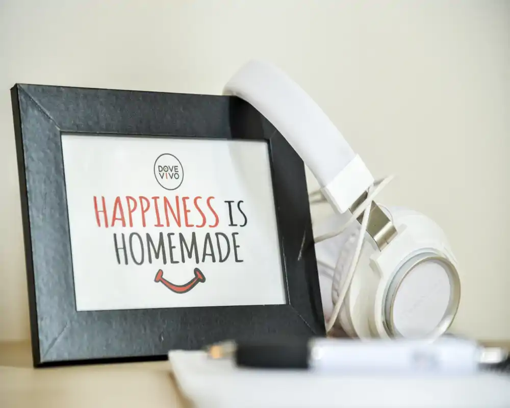 Gros plan d'une mise en scène sur table avec un cadre indiquant « HAPPINESS IS HOMEMADE » et un casque blanc ; photo décorative adaptée aux mises en scène lifestyle ou aux accessoires.