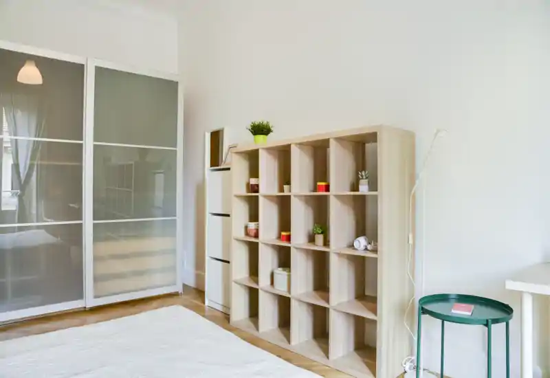 Chambre lumineuse et minimaliste avec matelas visible, grand placard coulissant à panneaux givrés et étagère cubique ouverte. L'espace paraît aéré et bien éclairé avec un mobilier moderne et sobre.