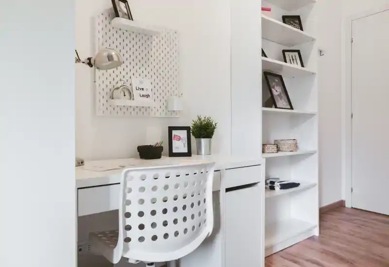 Coin bureau lumineux et minimaliste avec une chaise blanche perforée, des étagères intégrées et de simples éléments décoratifs — idéal pour un espace de travail à domicile.