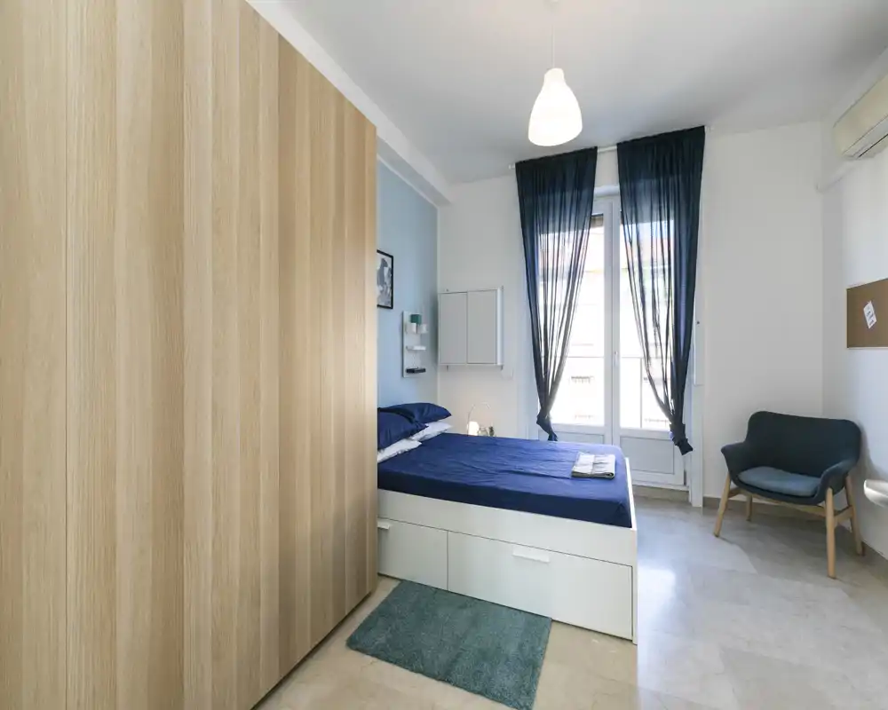 Dormitorio luminoso y bien presentado con cama doble, gran armario y ropa de cama azul; la luz natural crea un ambiente tranquilo.