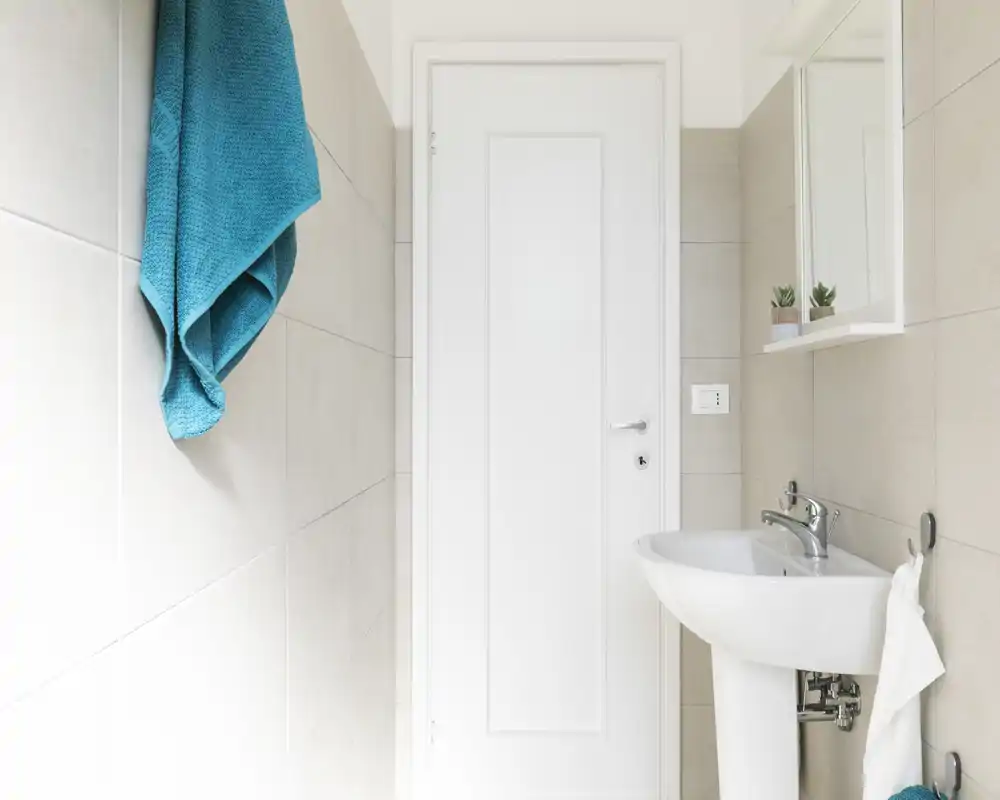 Baño pequeño y moderno con lavabo, espejo y una toalla turquesa que aporta un toque fresco. Limpio, luminoso y de estilo minimalista, ideal para anuncios de alquiler compactos.