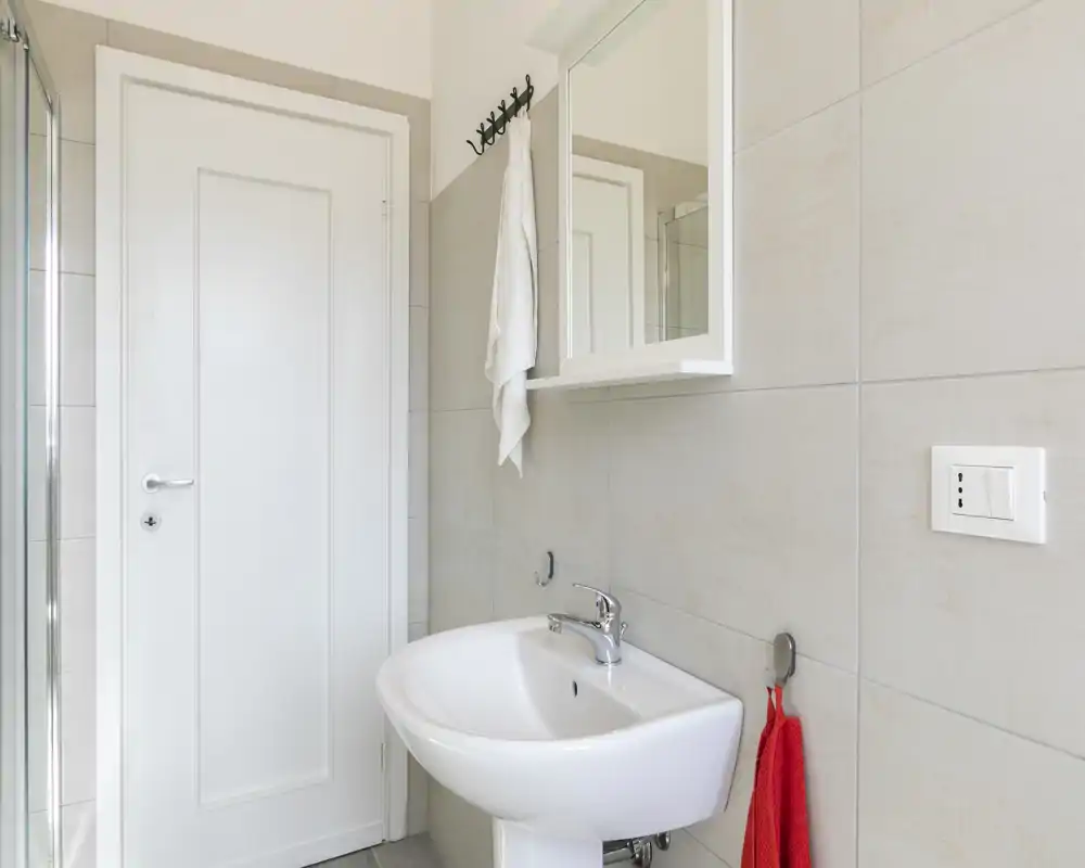 Baño moderno y limpio con mueble espejo en la pared, lavabo blanco y azulejos de tonos neutros. Espacio luminoso, adecuado para anuncios de alquiler.