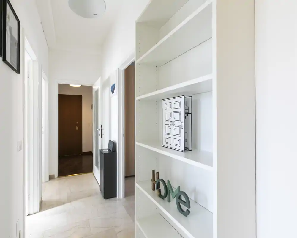 Vestíbulo luminoso y minimalista con estantería empotrada y paso despejado hacia la puerta principal, ideal para recibir invitados y guardar pequeños objetos.