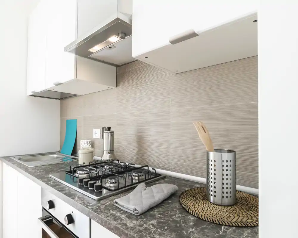 Encimera de cocina moderna y luminosa con placa de gas empotrada, campana extractora, fregadero y accesorios ordenados para un aspecto contemporáneo.
