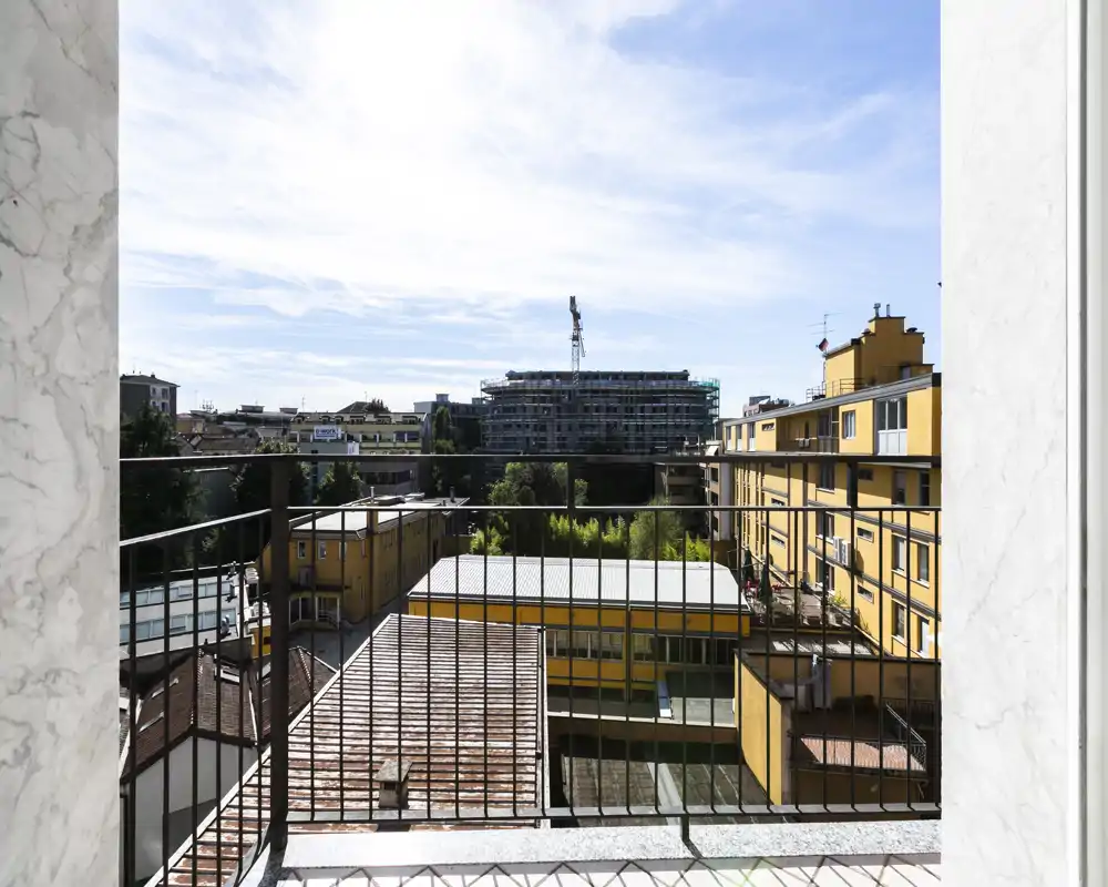Balcón soleado con barandilla metálica que da a edificios vecinos y una obra; vista urbana luminosa que destaca el espacio exterior.