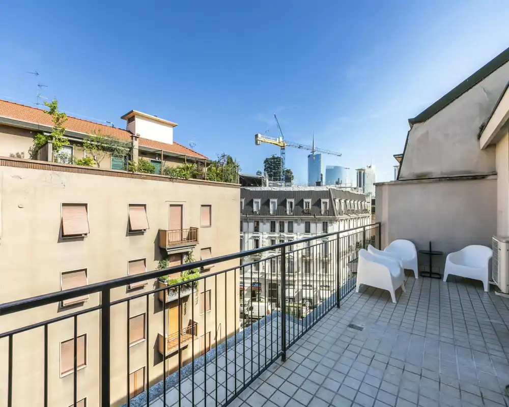 Balcón privado soleado con suelo de baldosas, asientos exteriores sencillos y agradable vistas a la ciudad — ideal para tomar un café por la mañana o relajarse al aire libre.