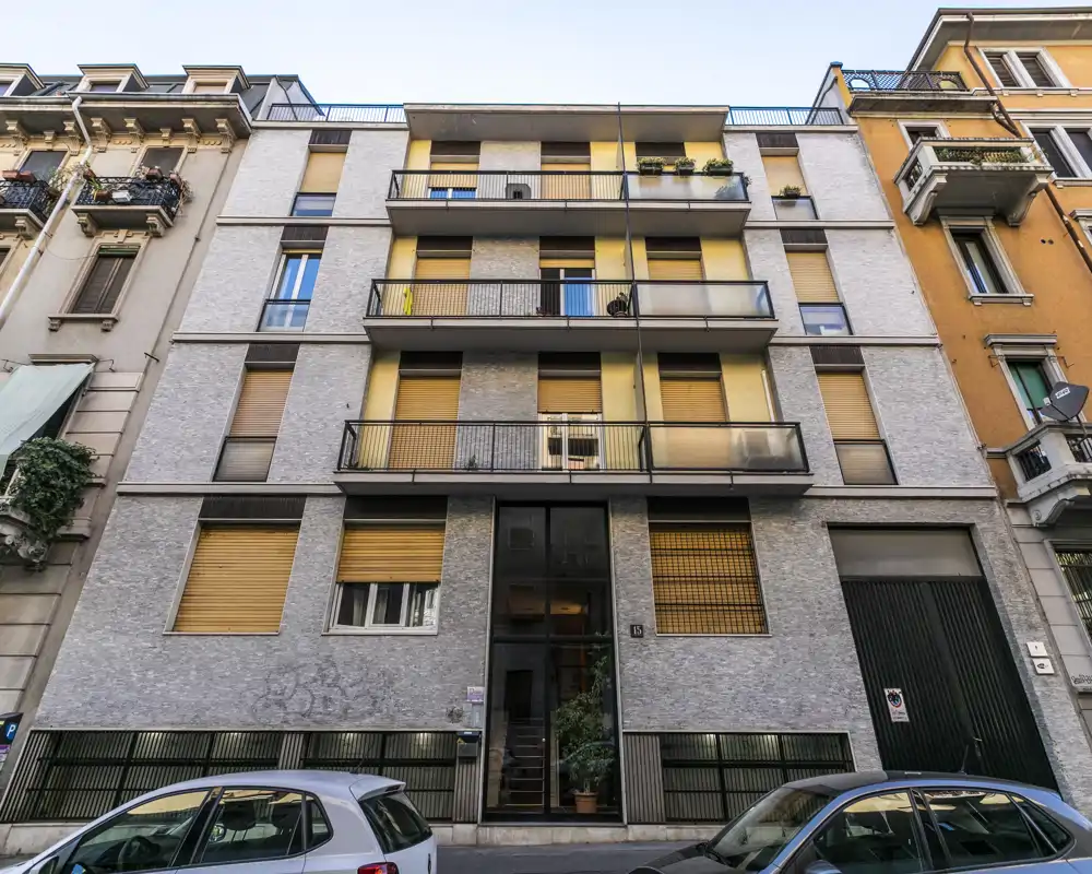 Foto exterior a nivel de calle de la fachada de un edificio de apartamentos de altura media con balcones y persianas, captada con luz natural. Adecuada para mostrar la vista exterior y el contexto del edificio.