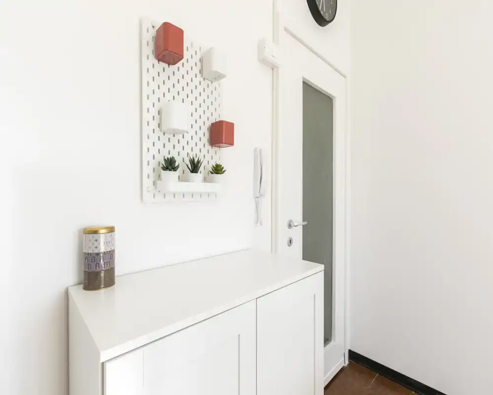 Entrada luminosa y minimalista con consola blanca, organizador de pared y portero automático — zona de acceso limpia y acogedora, ideal para el anuncio.