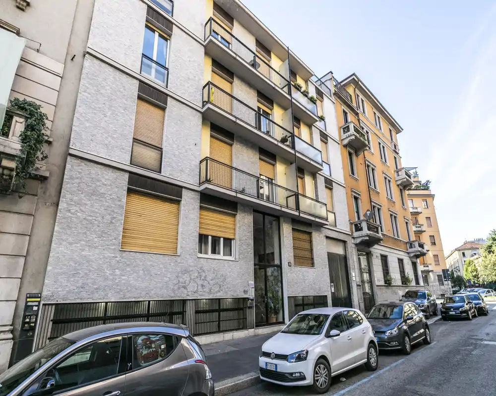 Vista exterior a nivel de calle de un edificio residencial de varias plantas con balcones y coches aparcados; foto clara a plena luz del día, adecuada para un anuncio de alquiler.