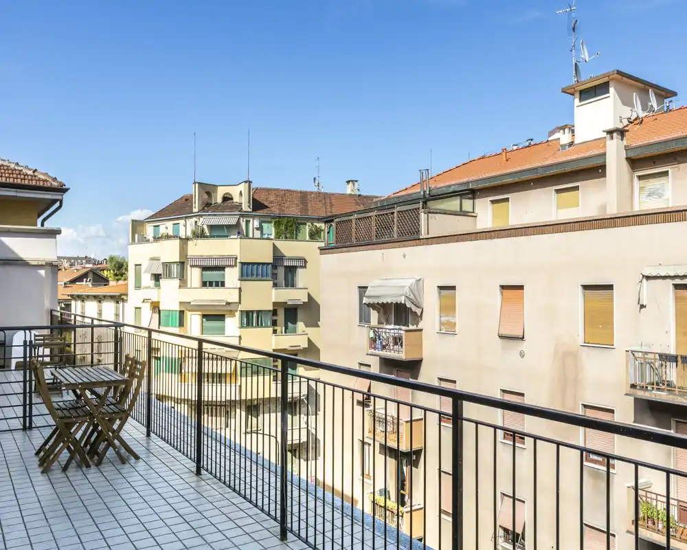 Balcón soleado amueblado con mesa y sillas con vistas a edificios cercanos: espacio abierto y luminoso ideal para el café matutino.