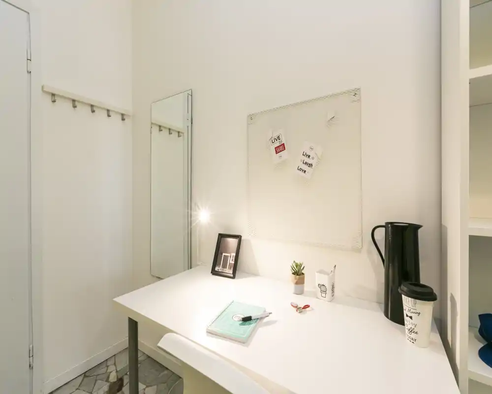 Área de escritorio luminosa y minimalista con superficie blanca, pequeña planta decorativa, foto enmarcada y lámpara de trabajo — ideal para concentrarse en un espacio compacto.