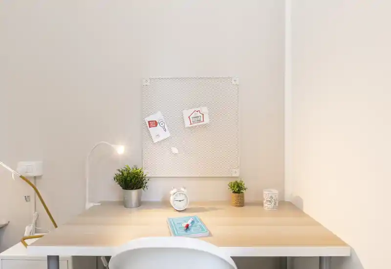 Bright, minimal desk area with a wooden tabletop, task lamp, small plants and a pinboard—ideal as a compact home office or study corner.
