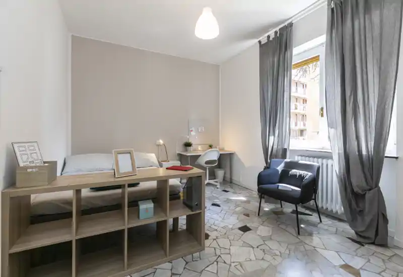 Bright, well-staged bedroom with a single bed, a bedside desk and a cozy armchair by the window. Natural light and neutral tones create a calm, welcoming atmosphere ideal for listings.