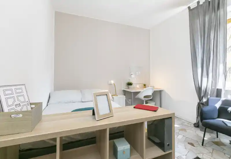 Dormitorio luminoso y minimalista con cama doble, pequeño escritorio y un sillón cómodo junto a la ventana. Tonos neutros y líneas limpias, perfecto para alquileres vacacionales.