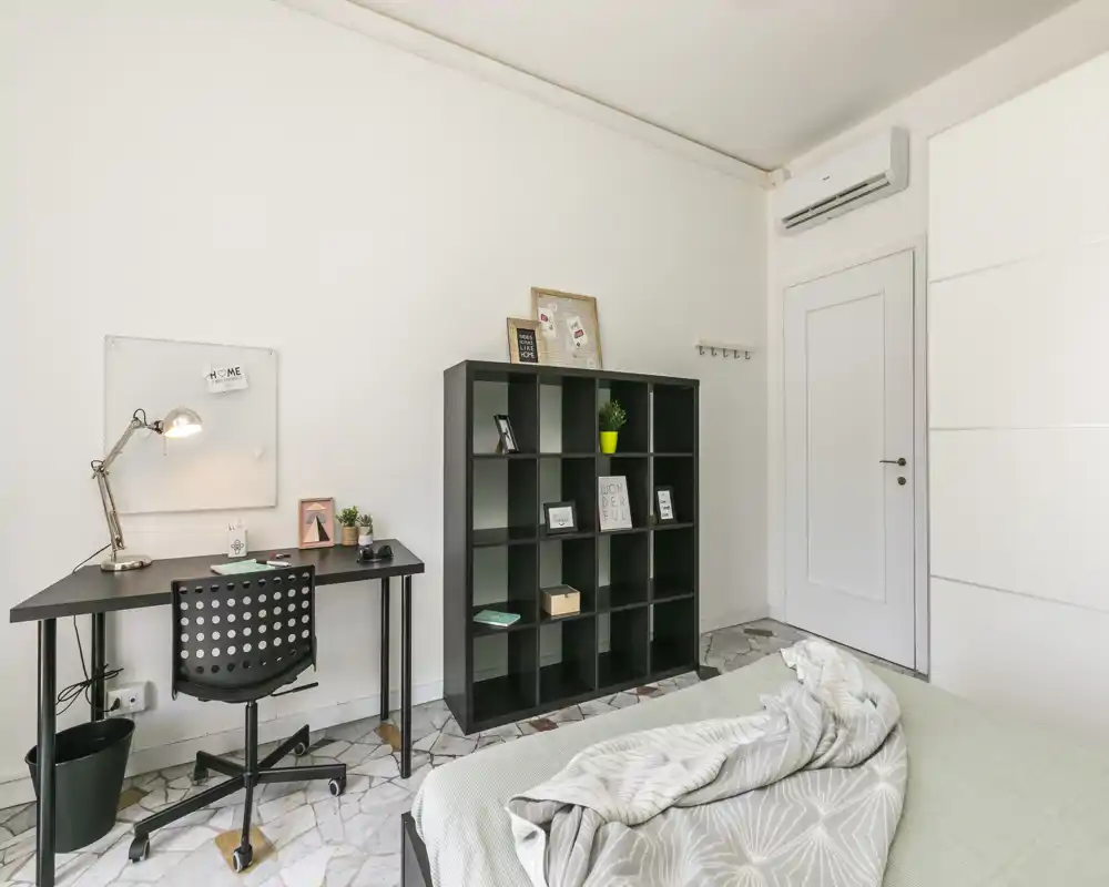Bright, modern bedroom with a visible double bed, tidy desk and shelving unit — ideal for a student or professional. Clean lines, neutral tones and good natural light create an airy, calm atmosphere.