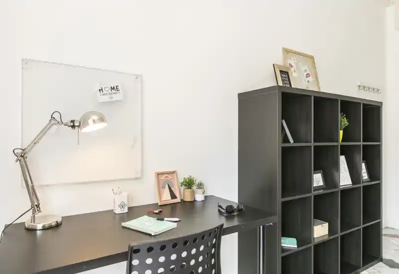 Bright, minimalist living/work nook with a black desk, task lamp and modular shelving—ideal for a compact home office or study corner.
