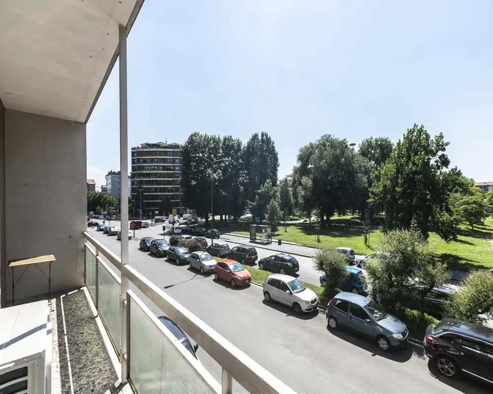 Balcón privado soleado con vistas a una calle arbolada y un parque; ideal para el café de la mañana con espacio para una mesa pequeña.