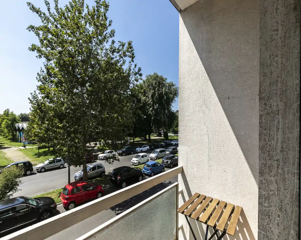 Balcón soleado con vistas a una calle arbolada y coches aparcados. Pequeña mesa plegable de madera en el balcón para disfrutar del exterior.