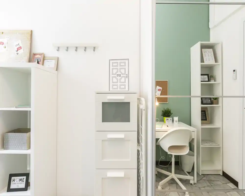 Rincón de trabajo luminoso y compacto con escritorio, silla giratoria blanca, estanterías y detalles decorativos — ideal para estudiar o trabajar a distancia.