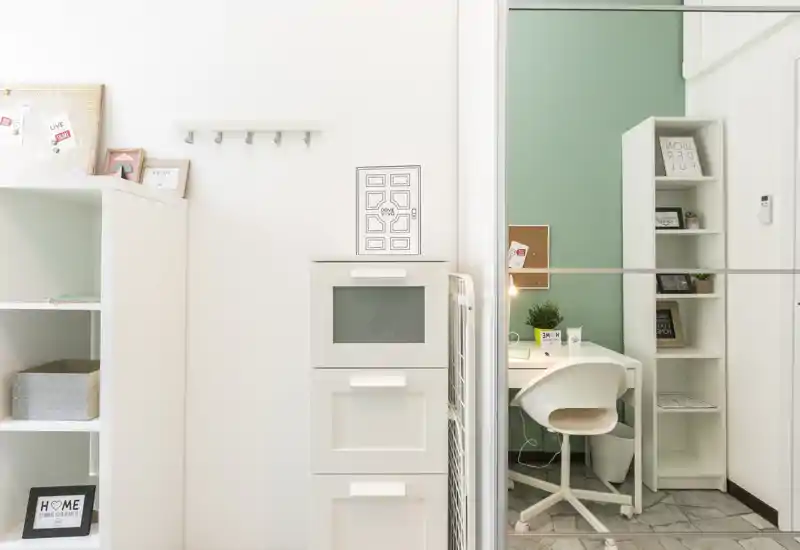 Bright, compact workspace corner with a desk, white swivel chair, shelving and decorative accents — ideal for studying or remote work.