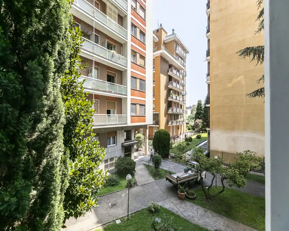 Vista luminosa del patio desde un balcón que da a un jardín comunitario con árboles, senderos y edificios cercanos.