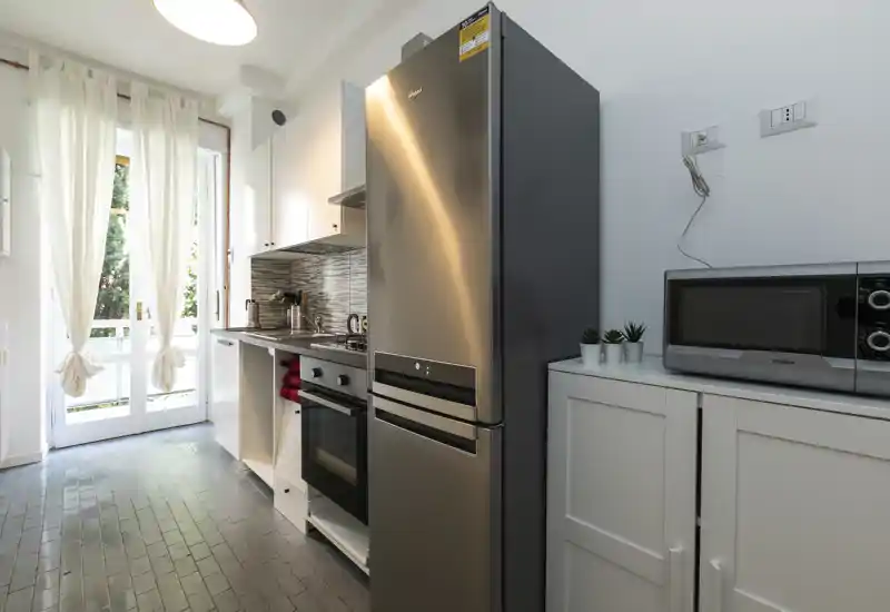 Modern galley kitchen with stainless-steel fridge, oven and microwave; bright natural light from the French doors and a clean, contemporary finish.