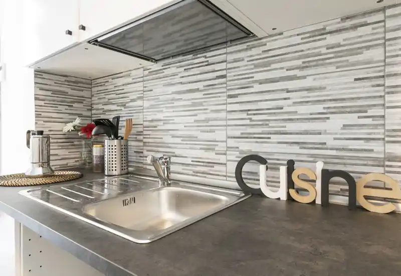 Bright, modern kitchenette with a stainless-steel sink, patterned tiled backsplash and neatly arranged utensils — compact and well-styled for short-stay rentals.