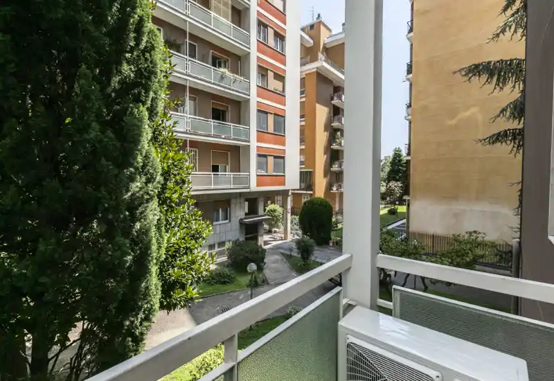 Sunny balcony overlooking a quiet residential courtyard with mature trees and neighboring apartment buildings — ideal for morning coffee.