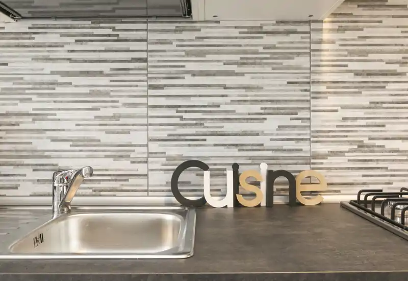 Modern kitchen counter with a stainless steel sink, gas hob and decorative wooden letters on a textured tile backsplash — bright, tidy and styled for photographs.