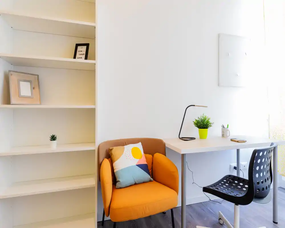 Angolo living luminoso e moderno con una poltrona arancione confortevole, cuscini decorativi e una scrivania ordinata con luce naturale — ideale per leggere o lavorare da casa.