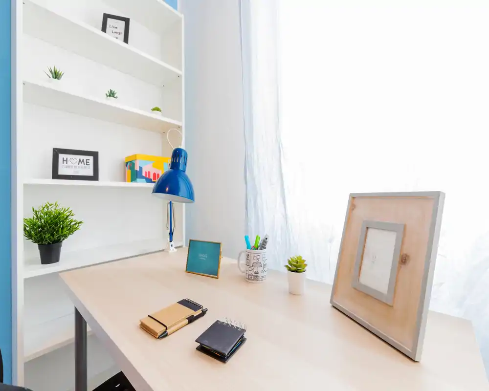Bright desk area with shelving, decorative plants and framed prints — a tidy home office/working corner ideal for listing photos.