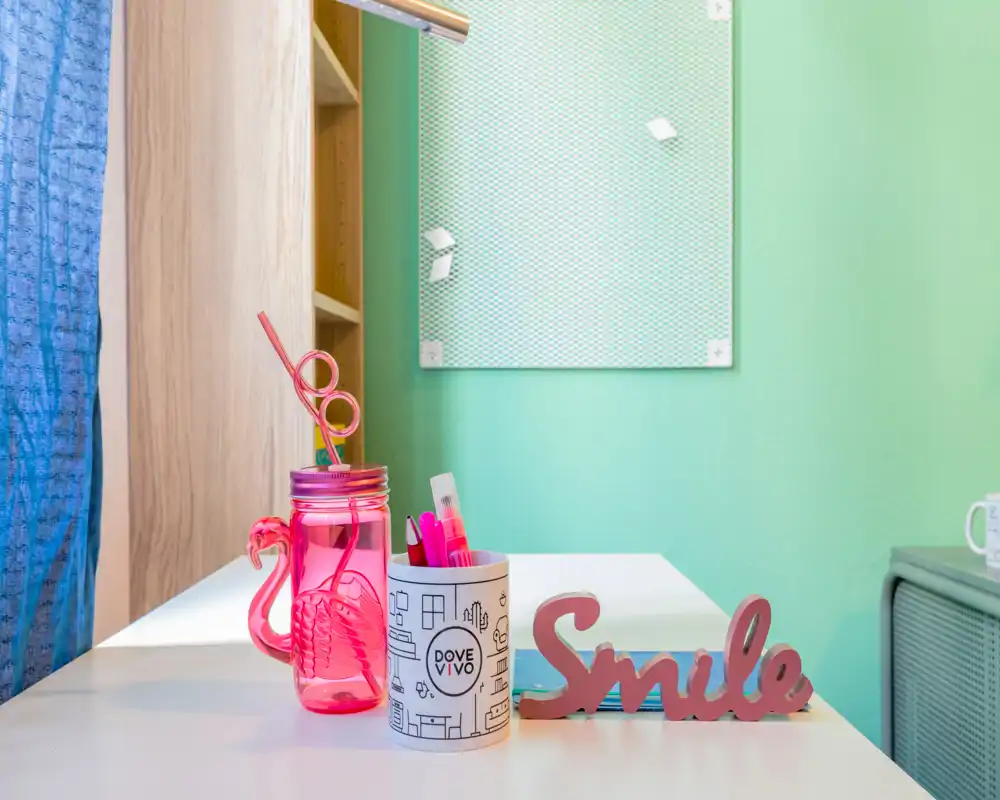 Rincón de escritorio luminoso y colorido con accesorios decorativos: tarro rosa, portalápices y un letrero "Smile" — ideal para mostrar un rincón acogedor.