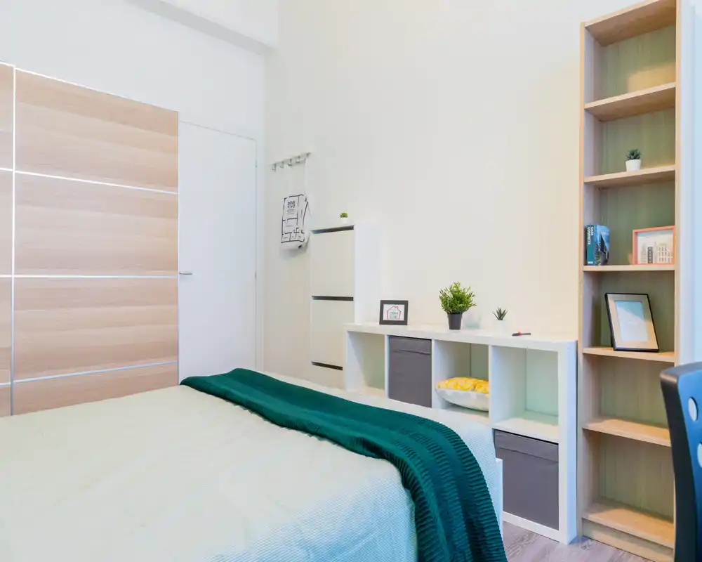 Dormitorio moderno y luminoso con cama bien hecha, manta verde y estanterías minimalistas — líneas limpias y luz natural que crean un ambiente relajante.