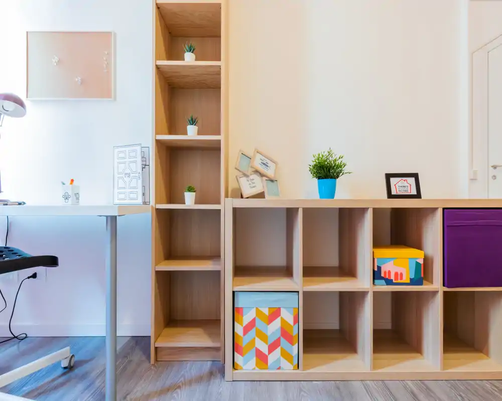 Zona giorno luminosa e moderna con scaffalature modulari in legno, scatole decorative e una piccola scrivania — uno spazio pulito e ben illuminato ideale per rilassarsi o lavorare.