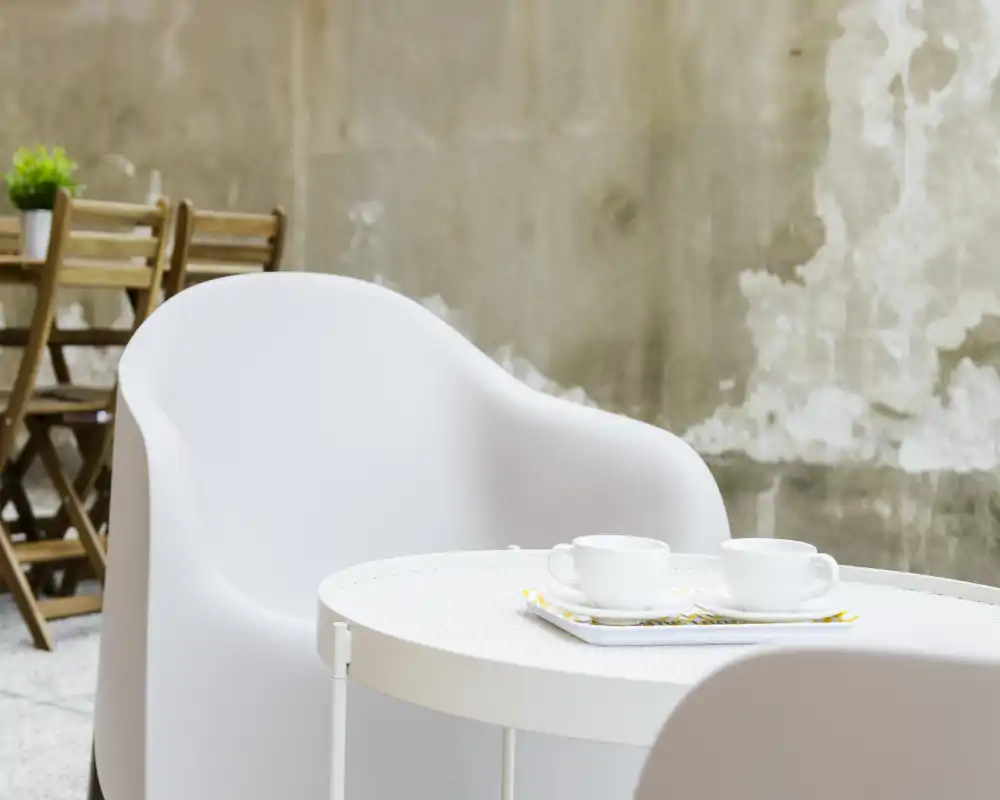 Piccolo angolo esterno con tavolino e sedie bianche moderne, due tazze su un vassoio e parete rustica sullo sfondo — perfetto per un caffè mattutino sulla terrazza.
