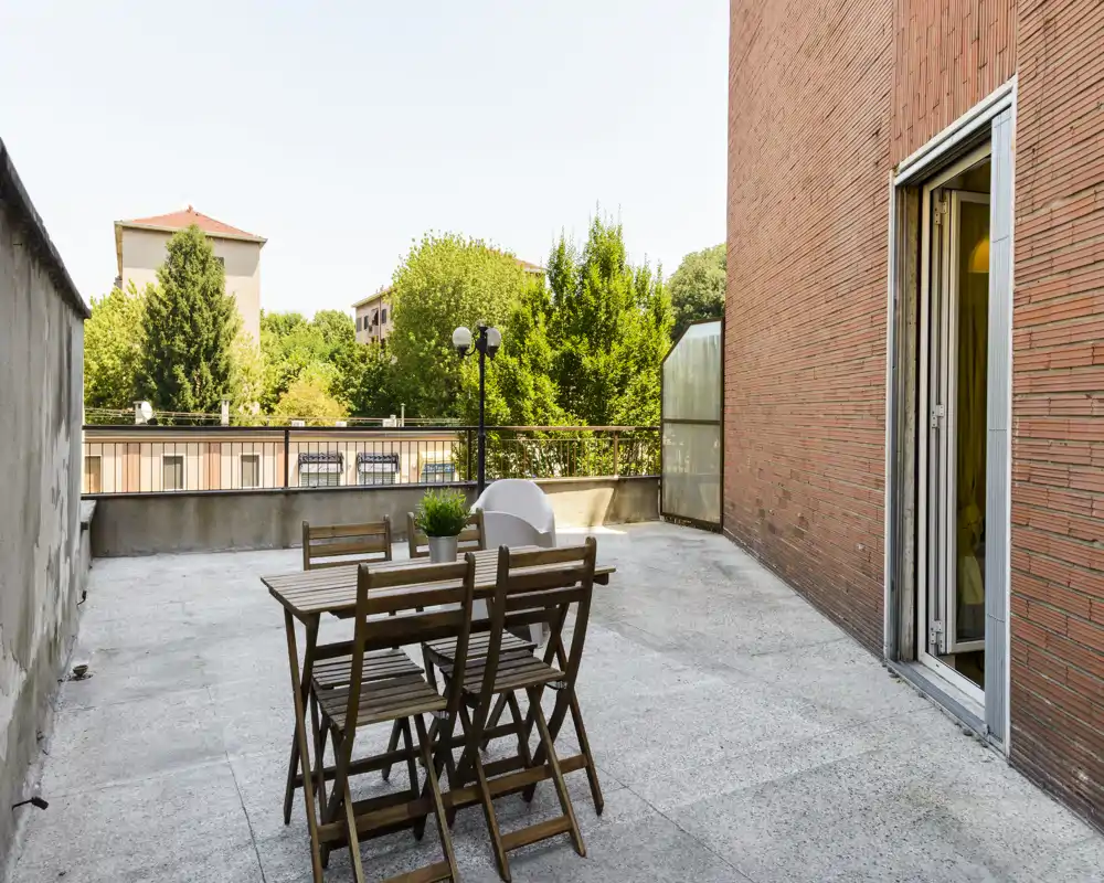 Terrazza privata soleggiata con tavolo e sedie in legno e vista sul verde cittadino — ideale per pranzi all'aperto o momenti di relax.