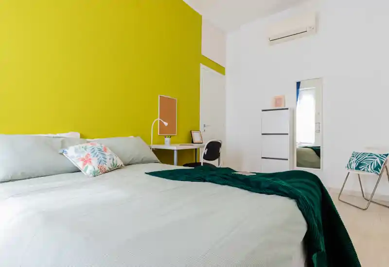 Dormitorio moderno y luminoso con cama grande, pared verde de acento y escritorio ordenado — aireado y acogedor para estancias cortas.