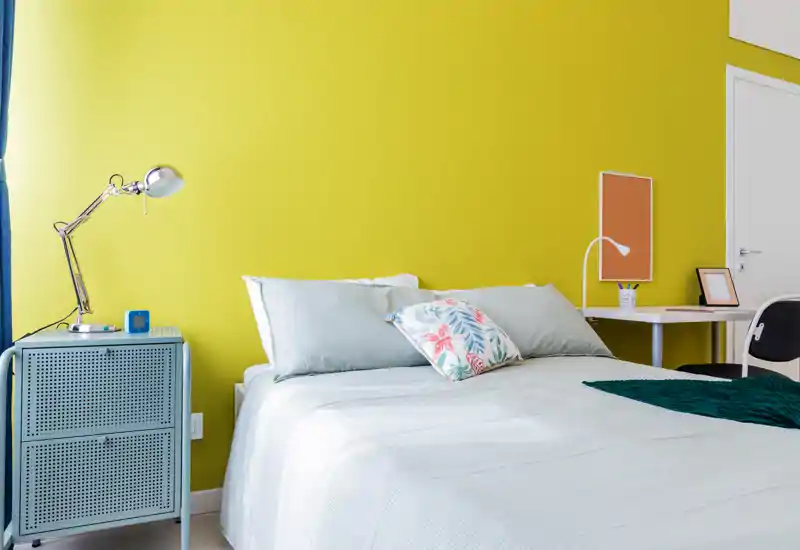Dormitorio moderno y luminoso con cama doble bien hecha, cojín decorativo y mesilla/escritorio coordinados — ideal para anuncios de alquiler que destaquen confort y estilo.