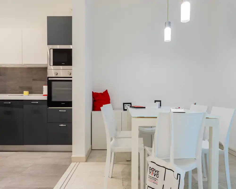 Zona de comedor moderna y luminosa en un espacio abierto junto a la cocina, con mesa blanca, sillas, lámparas colgantes y decoración minimalista.